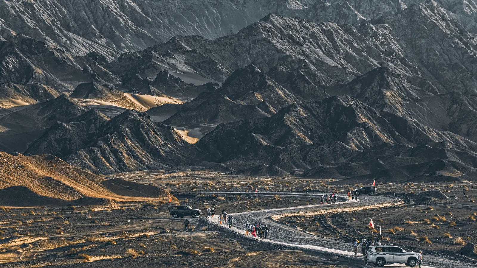 晨光下的荒野山地，一队参与者沿下方道路行进